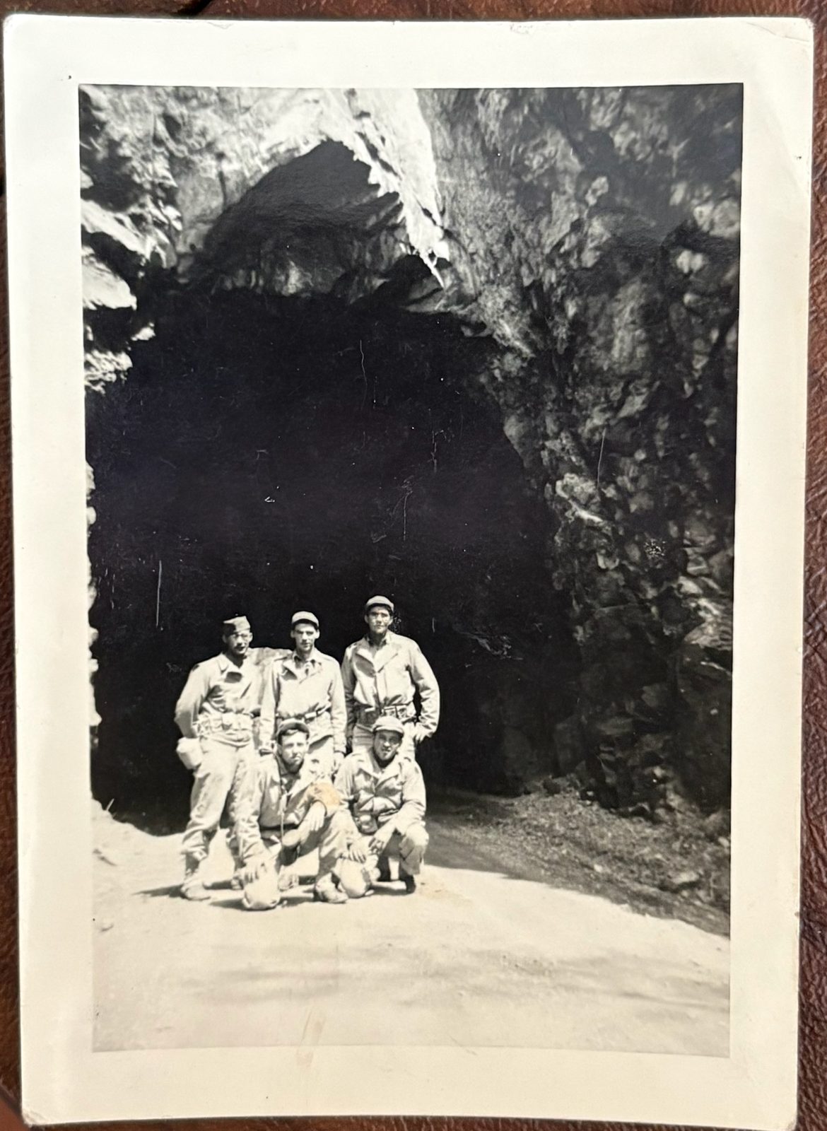 Five soldiers posed at the mouth of a large cave or quarry on a dirt road. Place and date uncertain.