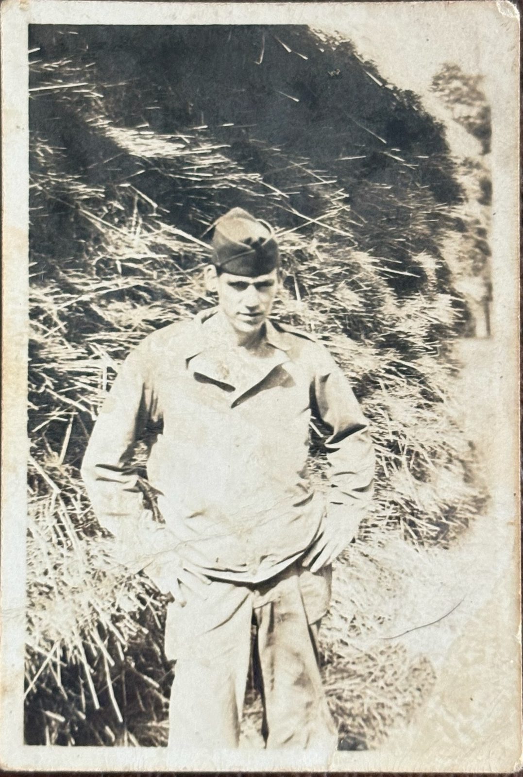 George in field jacket and overseas cap before a bank of hay. Mailed home and cleared by the Army censor (see the back).