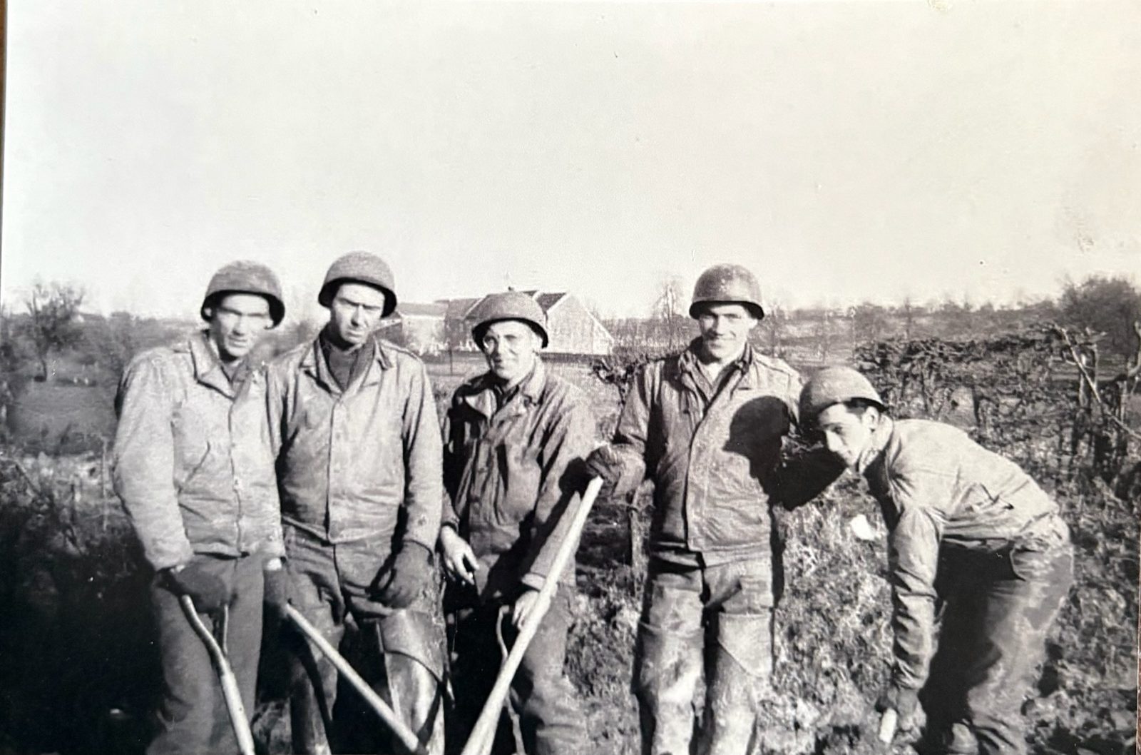George (far left) with his engineer squad and their shovels, a European farmhouse behind — exactly the road-and-bridge work the letters describe. In a letter from this stretch George mentions a photographer snapping them building a bridge.